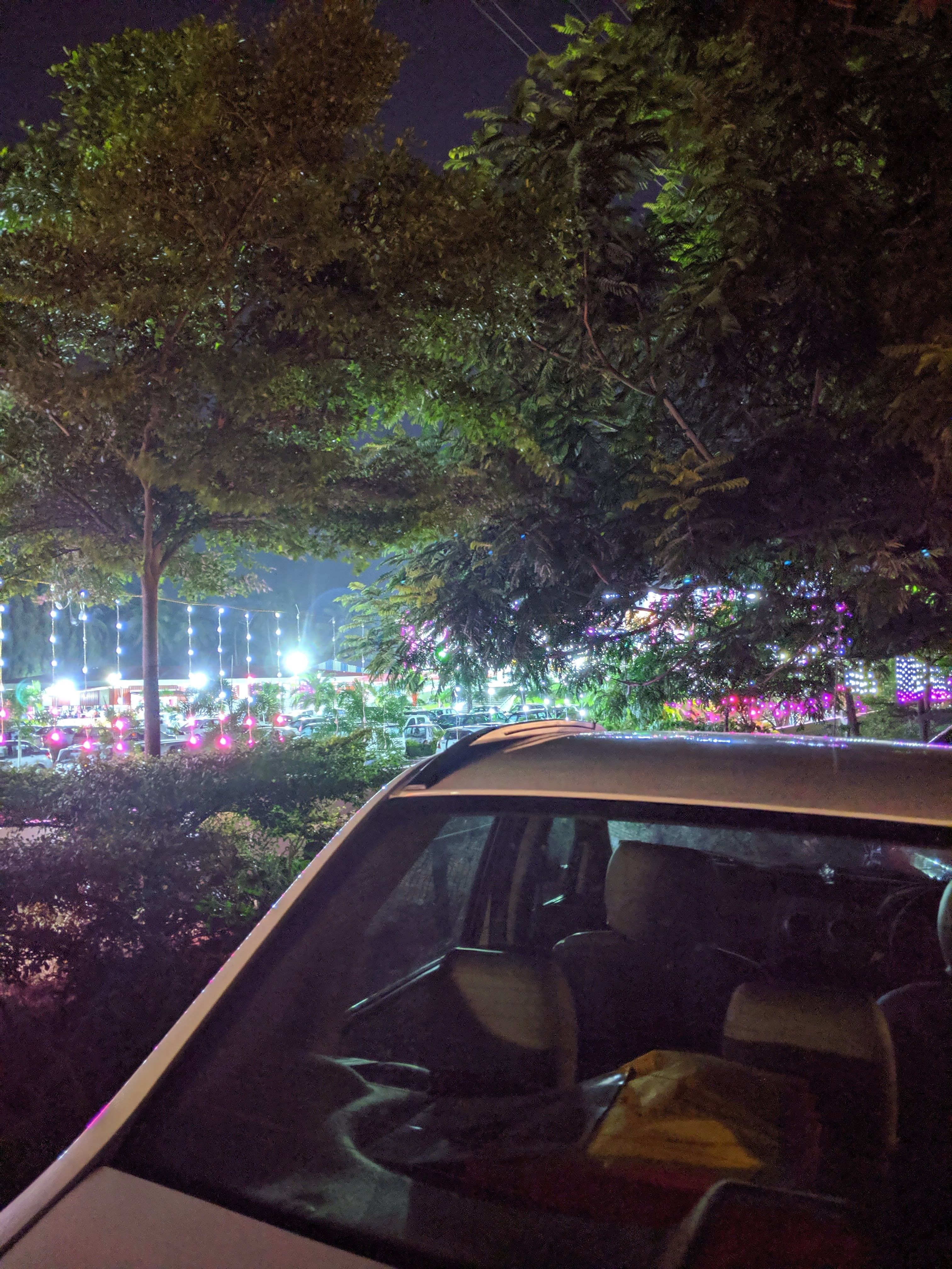 A brightly lit wedding hall with trees and cars parked outside