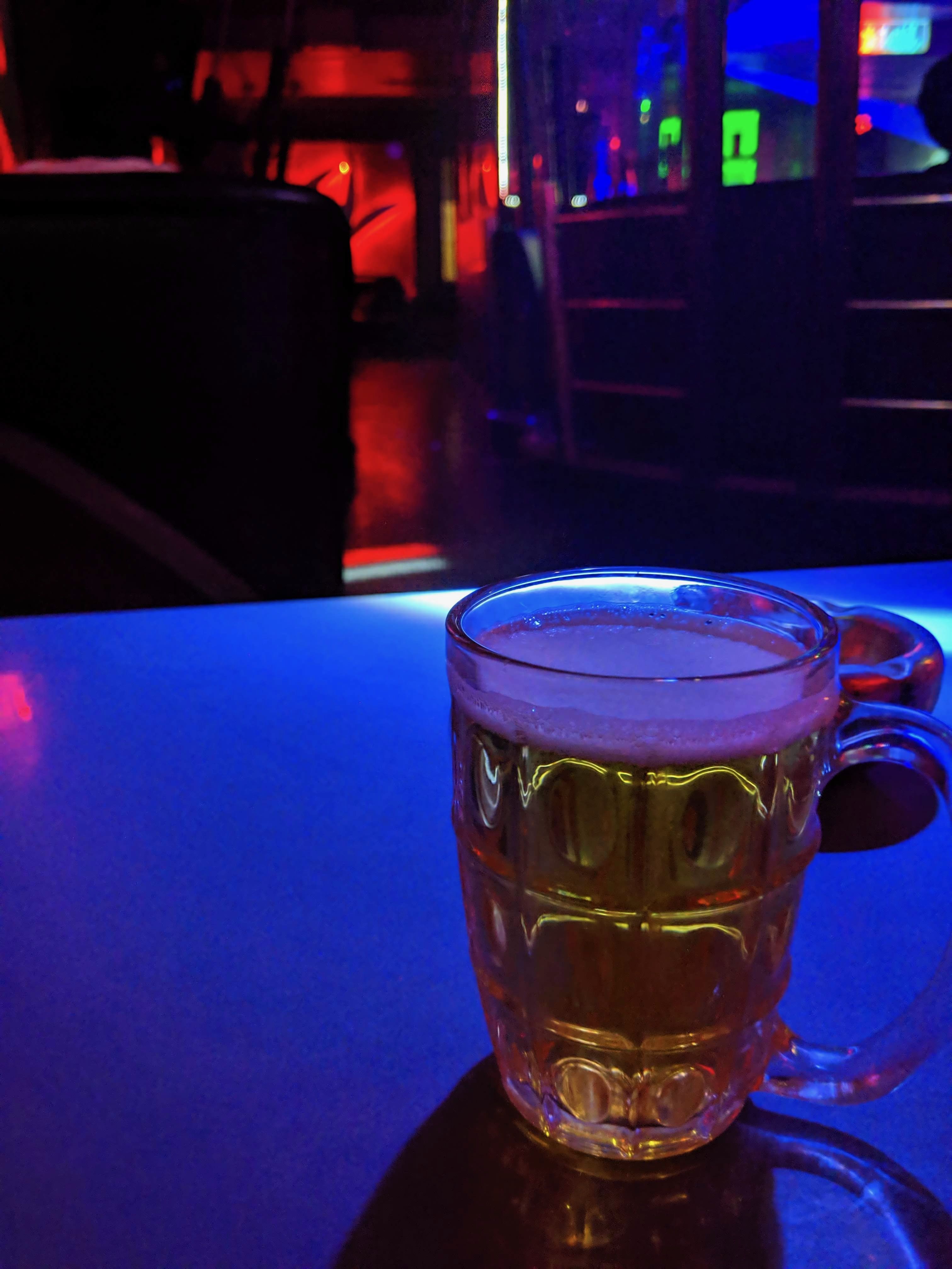 A glass filled with beer is on a table. It looks like a pub in there.